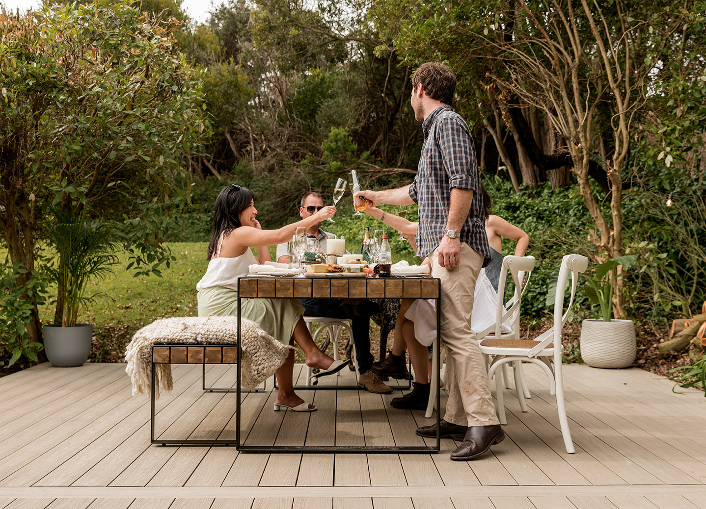 A group of people toasting at a table in a backyard.